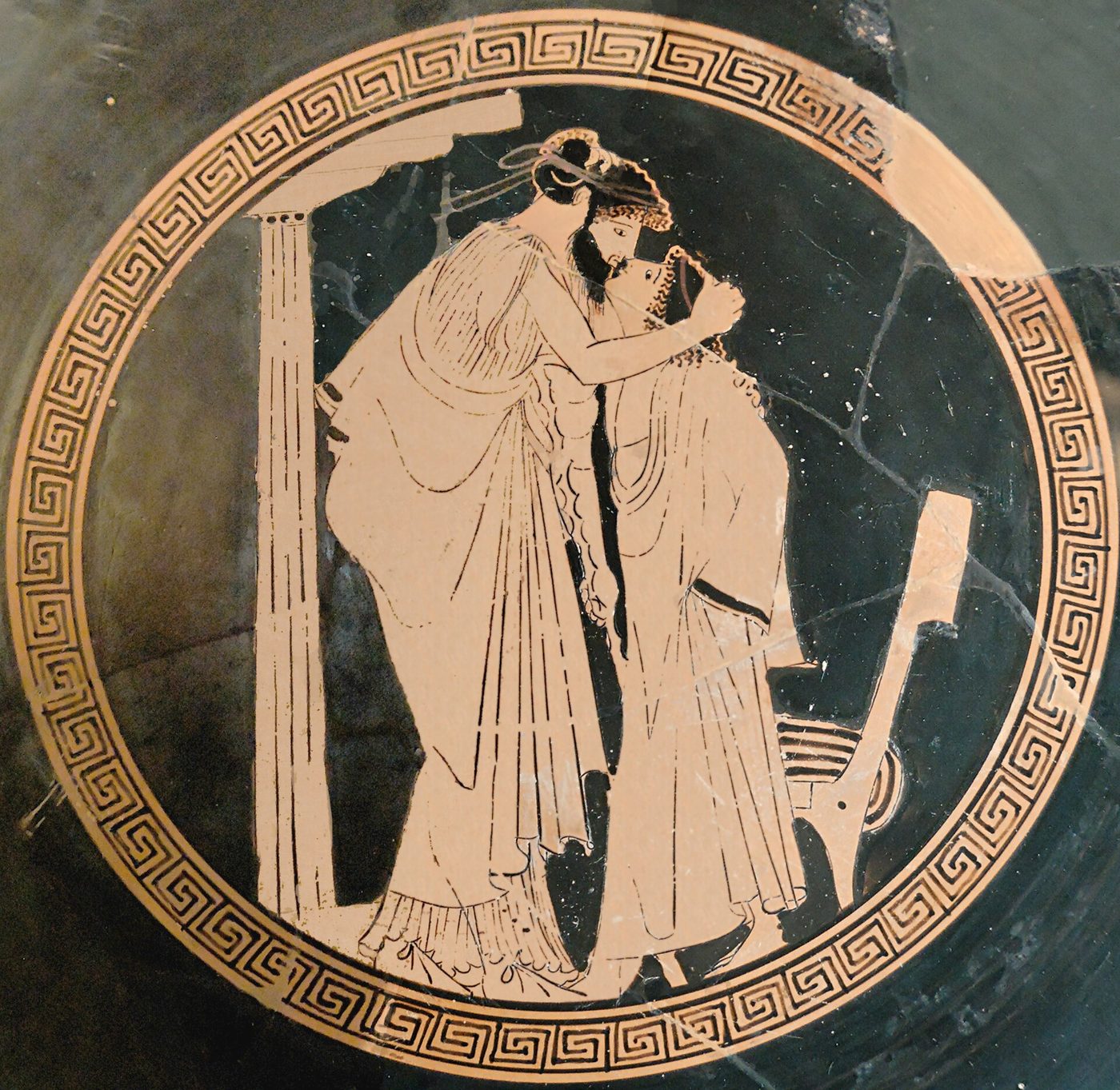 Interior de una copa griega de figuras rojas con dos figuras vestidas abrazándose junto a una columna