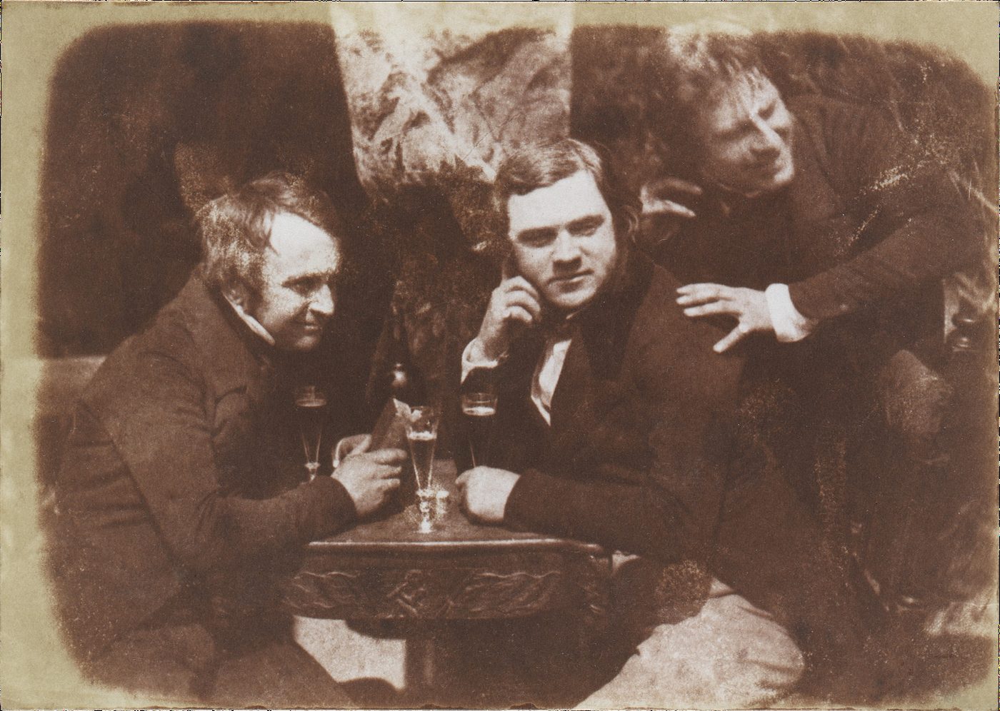 Calotipo de hacia 1844 con tres hombres sentados alrededor de una mesa pequeña con vasos, en actitud de brindis y conversación