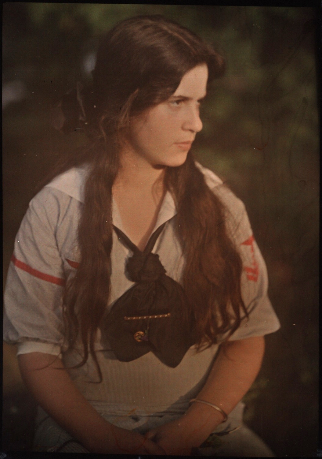 Autocromo de una joven de pelo largo y blusa clara sobre fondo oscuro, con los colores suaves y granulados