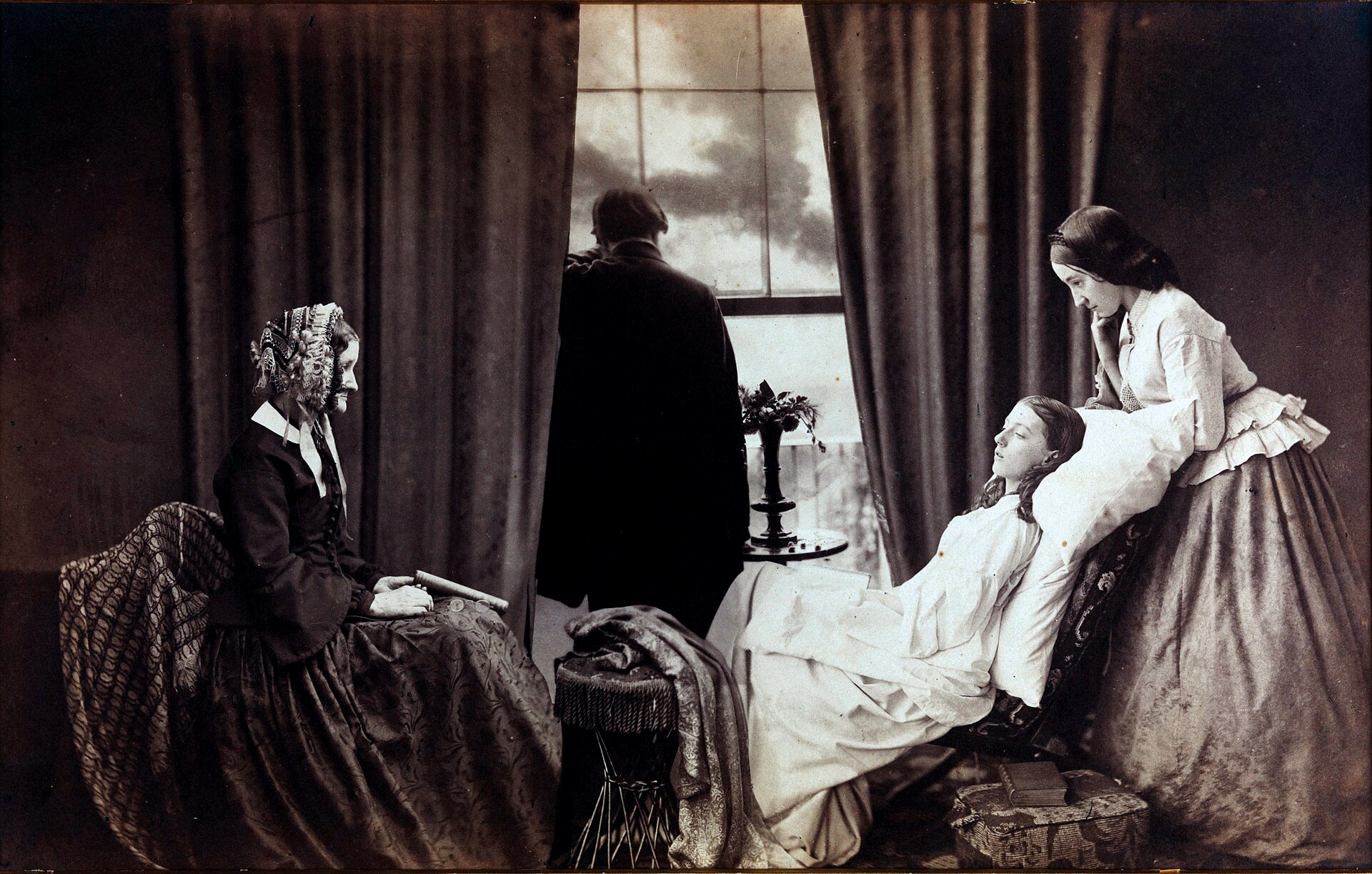 Fotografía de 1858 de una joven recostada en un sillón junto a una ventana, con dos mujeres y un hombre de espaldas velando su agonía