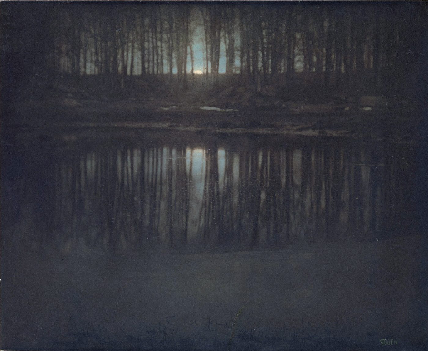 Fotografía pictorialista muy oscura y azulada de un estanque entre árboles con la luna reflejada en el agua