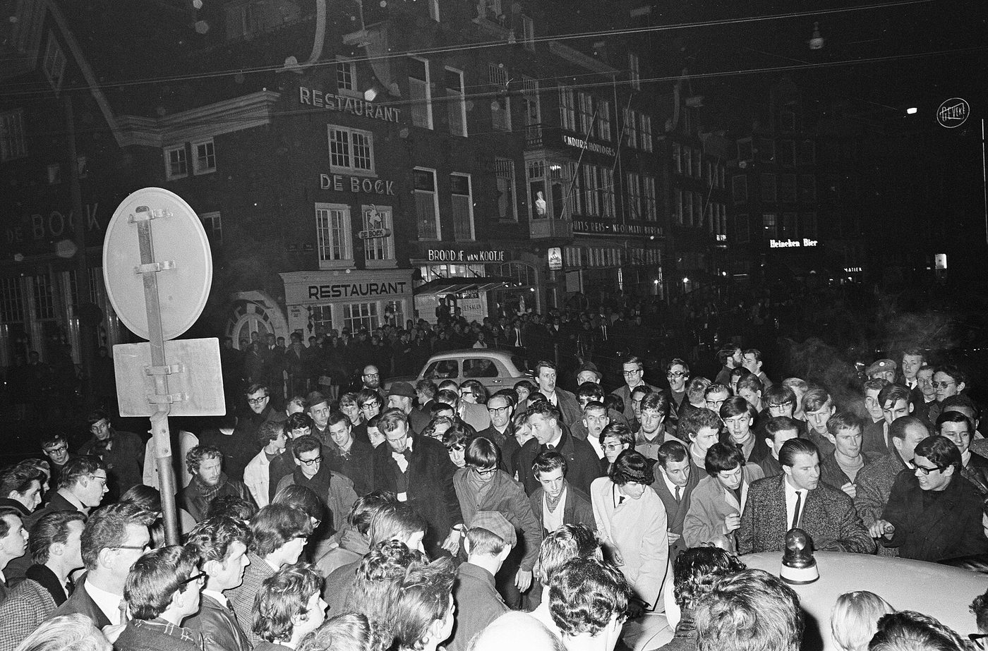 Fotografía nocturna de mediados de los años sesenta de una multitud juvenil apiñada en una plaza urbana frente a un cordón policial