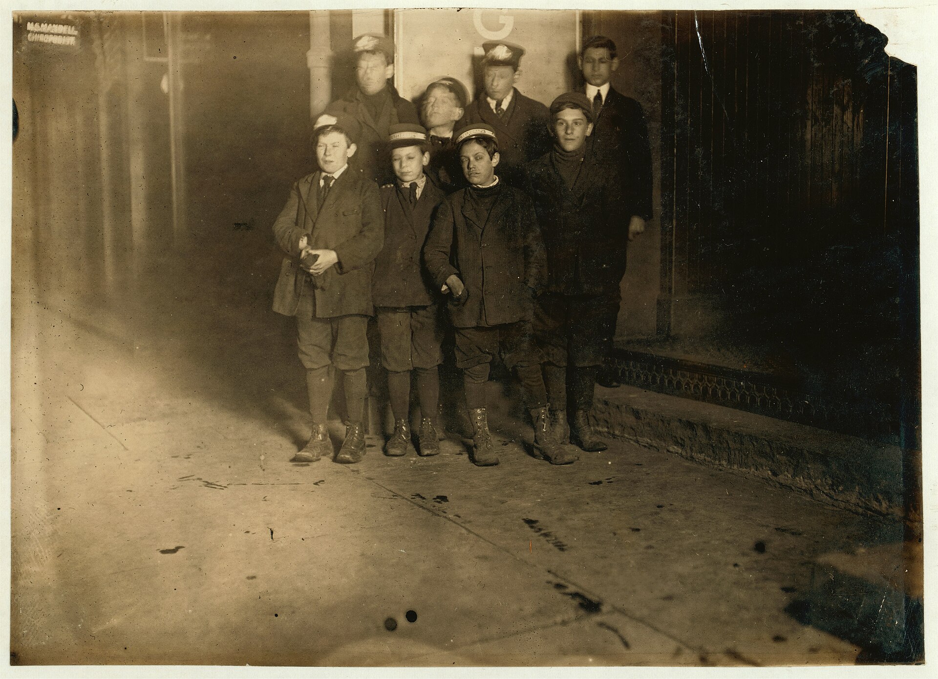 Fotografía nocturna de hacia 1909 de un grupo de chicos uniformados de mensajero en una calle oscura al terminar el turno
