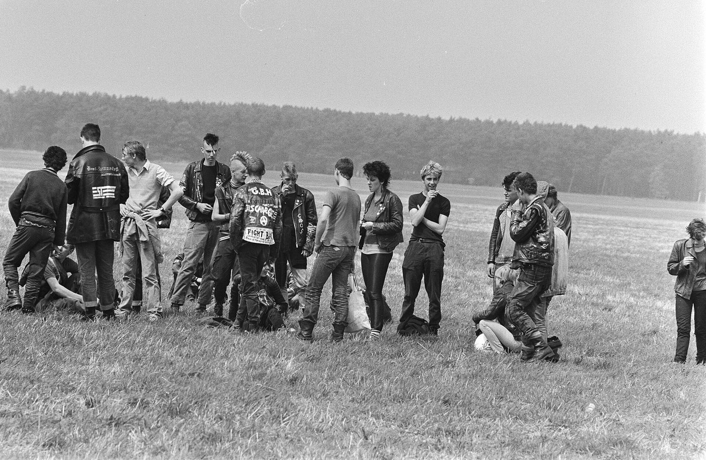 Fotografía en blanco y negro de principios de los años ochenta de un grupo de jóvenes punk con crestas y chaquetas de cuero sentados y de pie en una calle