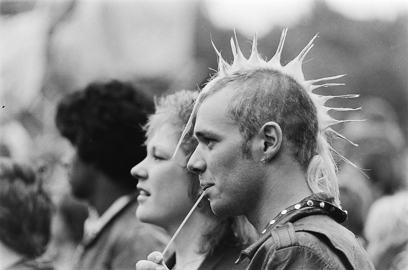 Fotografía de 1981 de dos jóvenes de perfil en un festival, uno con cresta de púas muy marcada y tachuelas al cuello