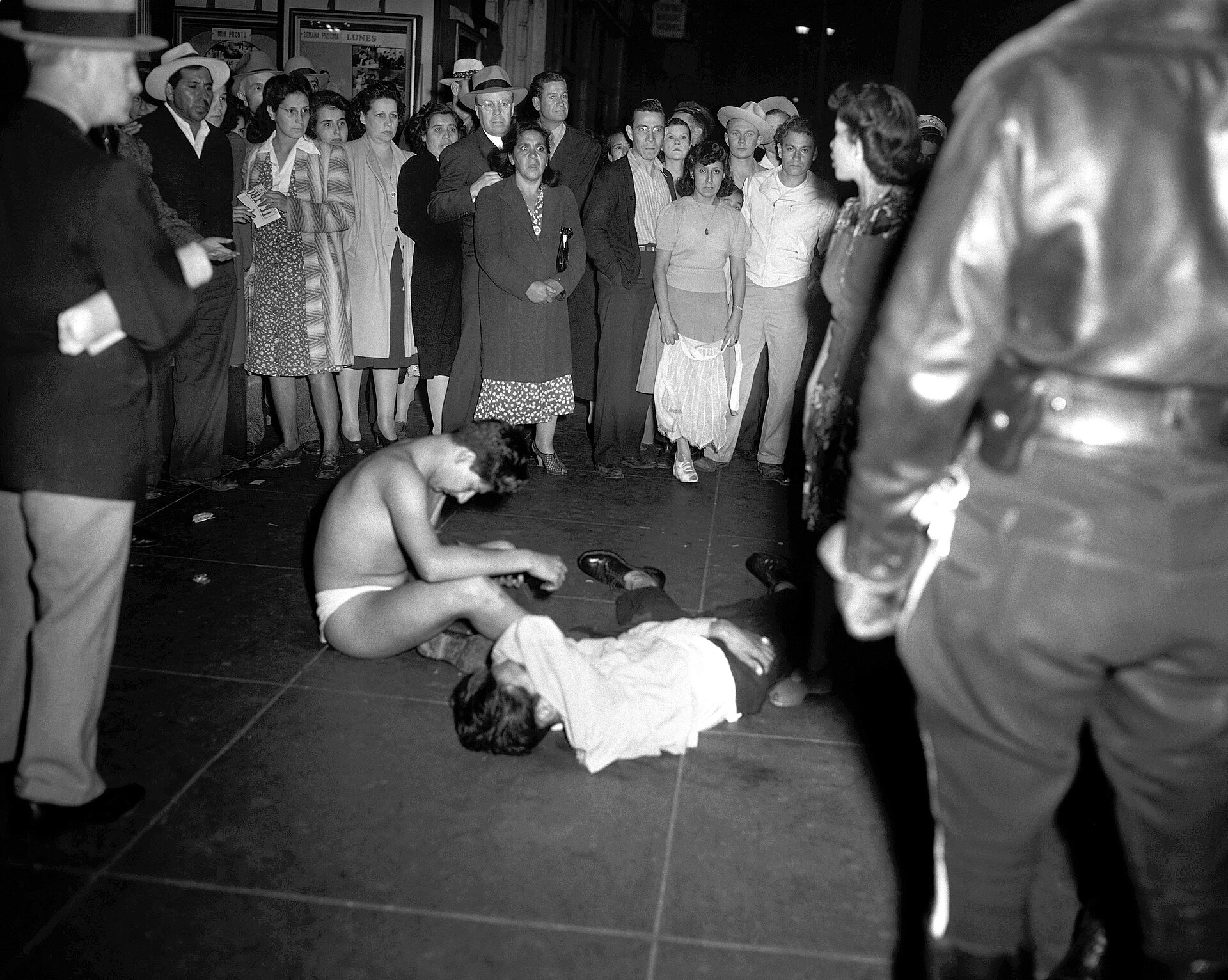 Fotografía de junio de 1943 de un hombre tendido en el suelo de una calle rodeado por un corro de curiosos y un policía